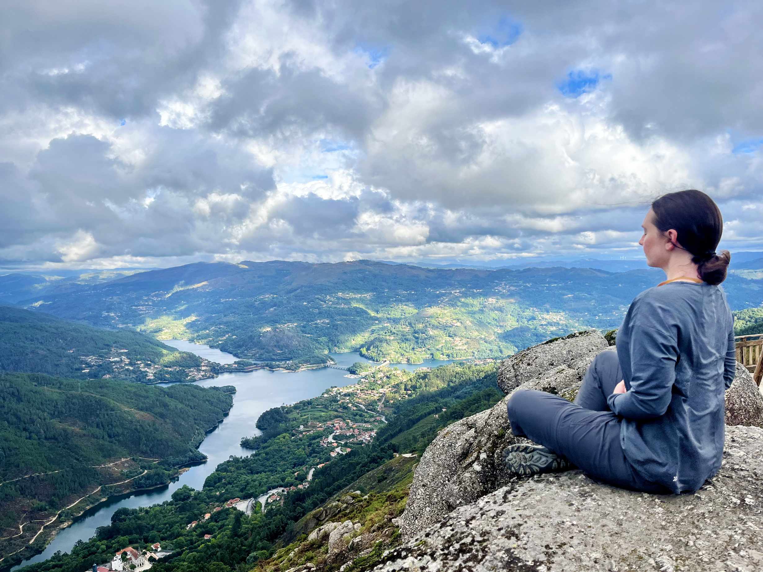 Anne sat on top of a mountain meditating looking down onto hills and a lake